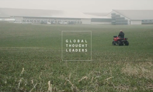 Dairy farmer driving an ATV through a field behind freestall barns.