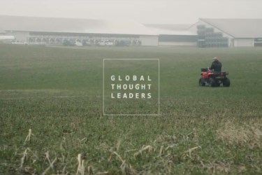 Dairy farmer driving an ATV through a field behind freestall barns.