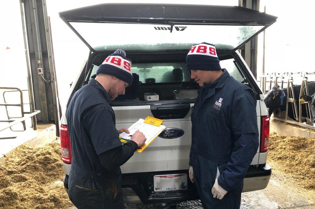 Two A.I. technicians discuss data report behind a truck.